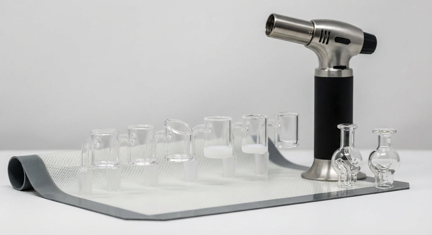Close-up of different quartz banger shapes lined up on a silicone dab mat next to a torch and carb caps