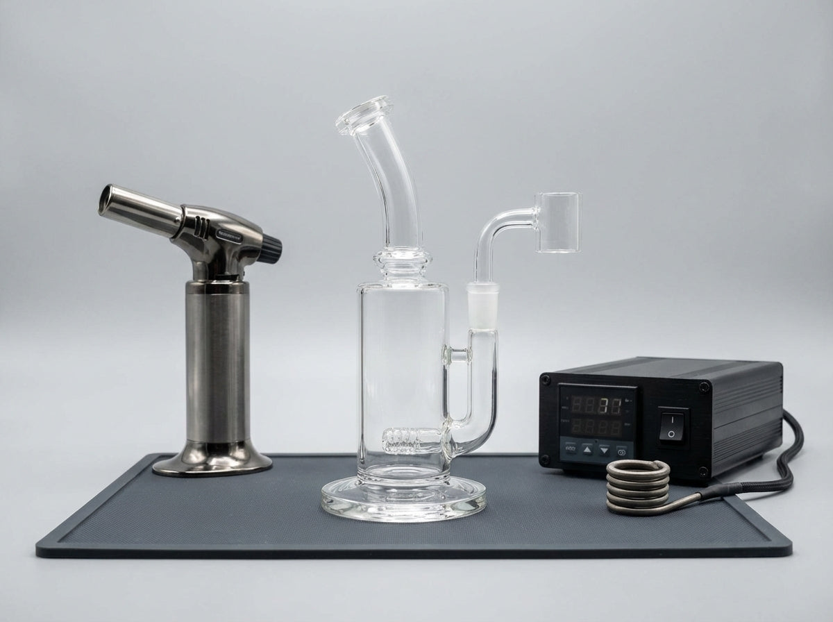 Close-up of a dab rig on a silicone dab mat, with a torch on one side and an e-nail controller box and coil on the other